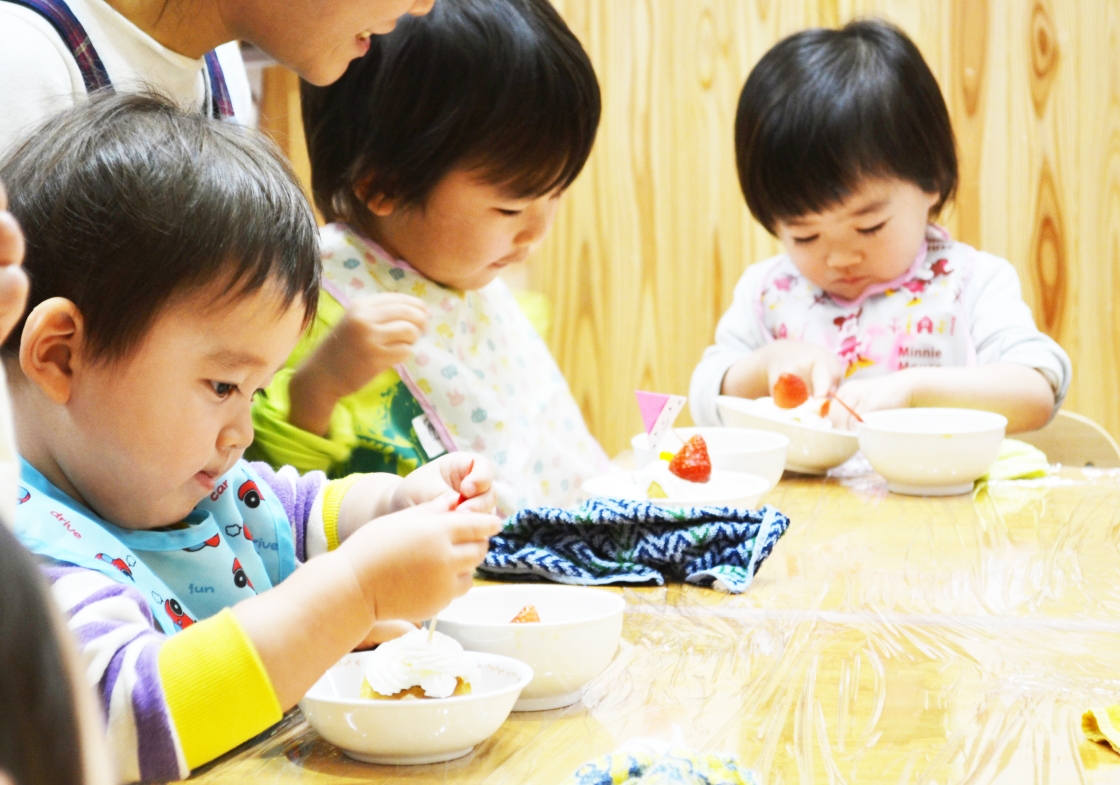 子ども達が好きな果物を選んでカップケーキに盛り付け、保育スタッフはその様子を見守ります。